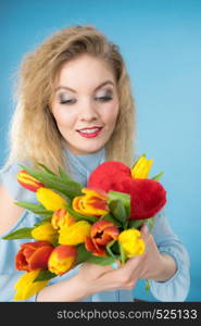 International womens or valentines day. Attractive happy woman blonde hair fashion make up holding tulips bunch and red heart sign. On blue. Woman holds tulips and red heart