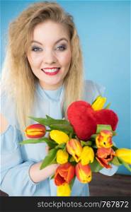 International womens or valentines day. Attractive happy woman blonde hair fashion make up holding tulips bunch and red heart sign. On blue. Woman holds tulips and red heart