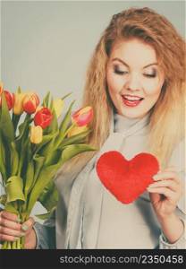 International womensm mothers or va≤nti≠s day. Beautiful woman blonde hair fashion make up holding tulips bunch and red heart sign. Fi<ered ima≥. Woman holds tulips and red heart