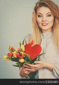 International womensm mothers or valentines day. Beautiful woman blonde hair fashion make up holding tulips bunch and red heart sign. Filtered image. Woman holds tulips and red heart