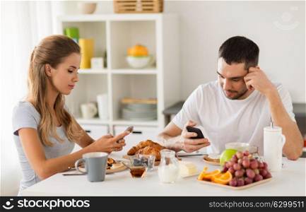 internet addiction, technology and people concept - couple with smartphones having breakfast at home. couple with smartphones having breakfast at home