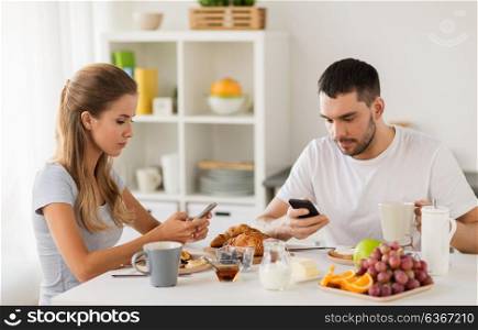 internet addiction, technology and people concept - couple with smartphones having breakfast at home. couple with smartphones having breakfast at home
