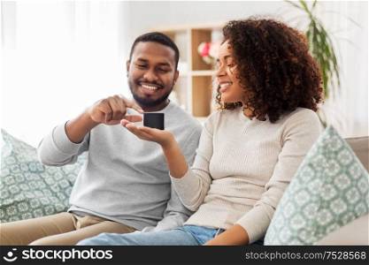 internet of things and technology concept - happy african american couple with smart speaker sitting on sofa at home. african american couple with smart speaker at home