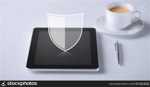 internet security, technology and cyber protection concept - virtual antivirus program shield icon over tablet pc computer with cup of coffee and pen. virtual antivirus program icon over tablet pc