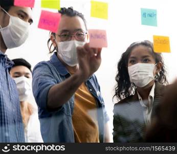 Interracial asian business team brainstorming idea at office meeting room after reopen due to coronavirus COVID-19 city lockdown. They wear face mask reduce risk to infection as new normal lifestyle.