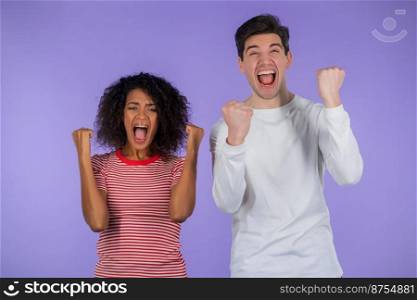 Interracial couple is very glad and happy, man and african woman shows yes gesture of victory, they achieved result, goals. Surprised excited happy family on purple studio background. Jackpot concept. Interracial couple is very glad and happy, man and african woman shows yes gesture of victory, they achieved result, goals. Surprised excited happy family on purple studio background. Jackpot concept.
