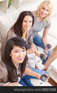 Interracial group of three beautiful young women friends at home drinking red wine together