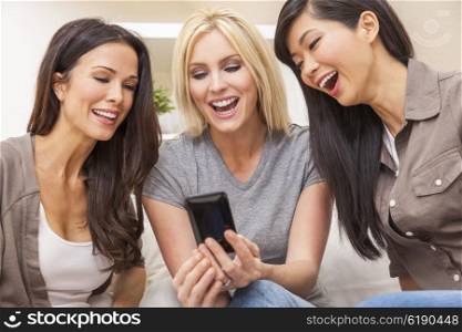 Interracial group of three beautiful young women friends at home laughing using a smart phone at home