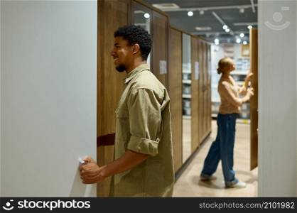 Interracial married couple at furniture shop. Man pulls out cabinet, woman looking for other sample. Married couple different nationally at furniture shop