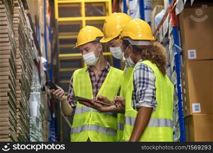 Interracial team Asian African and Caucasian work check goods use clipboard barcode scanner in distribution center. They wear face mask prevent from COVID-19. Storeroom warehouse inventory concept.