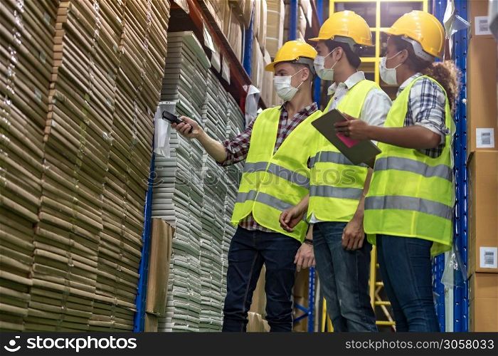 Interracial team Asian African Caucasian working on inventory use barcode scanner and digital tablet in distribution center. They wear face mask prevent from COVID-19. Warehouse and hygiene concept.