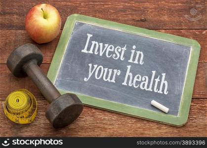 Invest in your health - slate blackboard sign against weathered red painted barn wood with a dumbbell, apple and tape measure