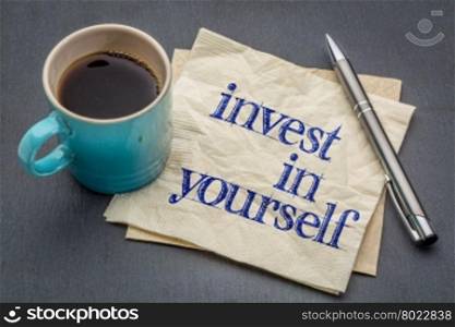 Invest in yourself advice or reminder - handwriting on a napkin with cup of coffee against gray slate stone background
