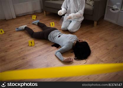 investigation and forensic examination concept - criminalist collecting evidence of murder of woman at crime scene fenced by police tape (staged photo). criminalist collecting evidence at crime scene
