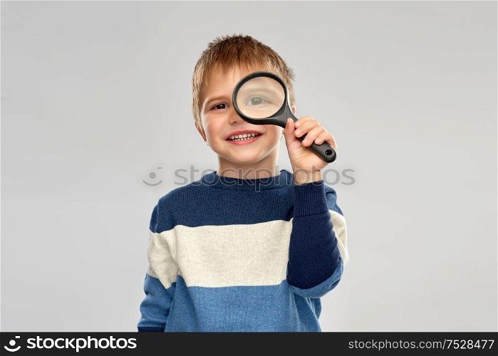 investigation, discovery and vision concept - smiling little boy looking through magnifying glass over grey background. little boy looking through magnifying glass
