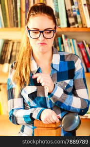 Investigation exploration education concept. Closeup funny student girl in library, woman in eyeglasses holding magnifying glass loupe