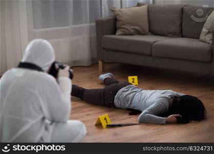 investigation, forensic examination and people concept - criminalist with camera photographing dead female victim body at crime scene (staged photo). criminalist photographing dead body at crime scene