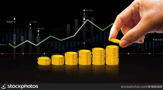 Investment concept, Hand putting gold coin to stack of coins with graph chart blurred on black background