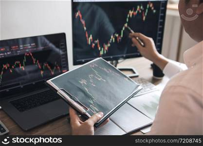Investor man analyzing the graph of the stock market using a pen pointing to the computer screen.