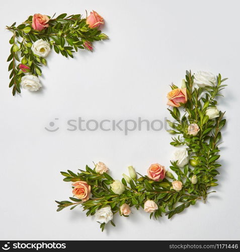 Invitation square corner frame from evegreen leaves branches on a light grey background with copy space. Flat lay. Valentine&rsquo;s Day concept.. Square greeting card with evergreen twigs and flowers.