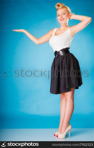 Inviting, showing and sharing concept. Pin up retro girl style. Blonde young full length woman with hand invitation gesture or copy space for text product on blue background in studio.