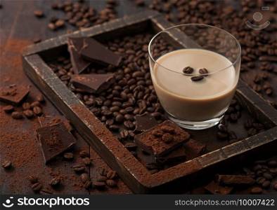 Irish cream baileys liqueur in glass with coffee beans and powder with dark chocolate in wooden tray on dark wood background. Top view