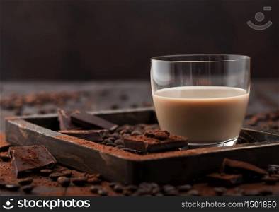 Irish cream baileys liqueur in glass with coffee beans and powder with dark chocolate in wooden tray on dark wood background. Space for text