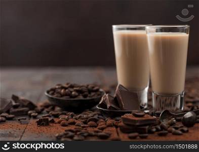 Irish cream baileys liqueur in shot glasses with coffee beans and powder with dark chocolate on dark wood background. Space for text