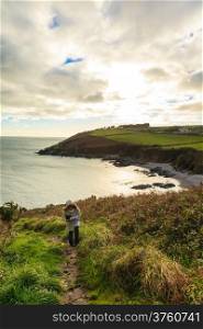 Irish landscape. Coastline atlantic ocean coast scenery cloudy blue sky, Church Bay County Cork, Ireland Europe. Woman female tourist walking