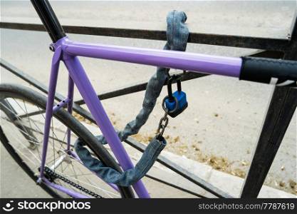 Iron chain and lock on a old bicycle of violet color. Locked bicycle at bicycle outdoor parking space. Iron chain and lock on a old bicycle of violet color