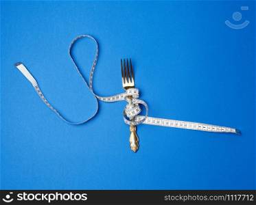 iron fork wrapped in a measuring tape on a blue background, top view