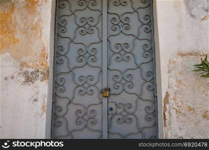 Iron gate with old fashioned metalwork pattern and textured wall background. Abandoned house exterior.