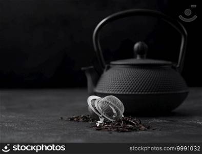 Iron japanese teapot with black loose tea with strainer infuser on dark background.