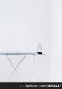 Iron on ironing board against white wall