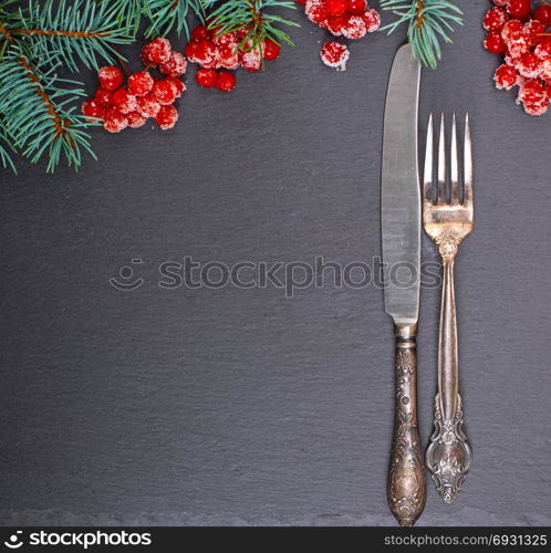 iron vintage fork and knife on a black background, decorated with a branch of spruce