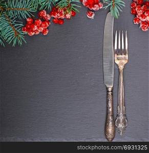 iron vintage fork and knife on a black background, decorated with a branch of spruce