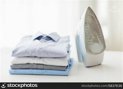 ironing, clothes, housework and objects concept - close up of iron and clothes on table at home
