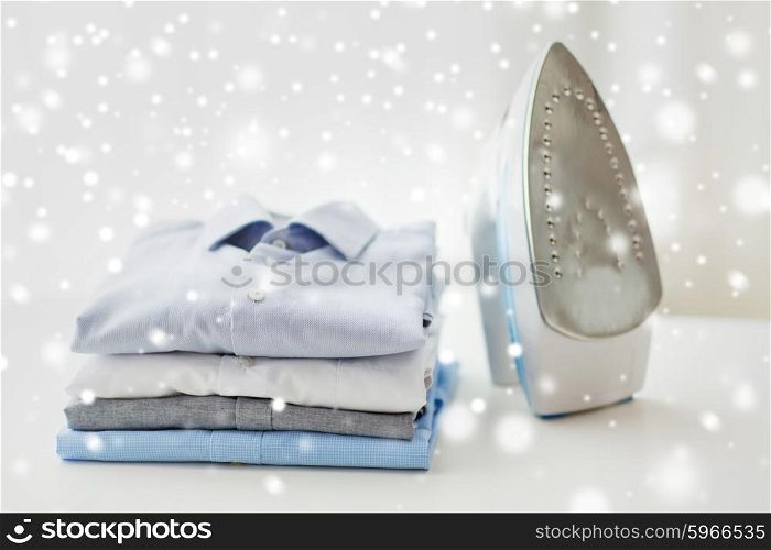 ironing, clothes, housework and objects concept - close up of iron and clothes on table at home over snow effect