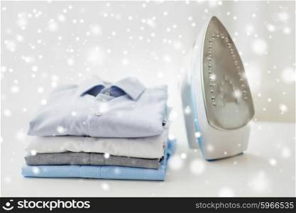 ironing, clothes, housework and objects concept - close up of iron and clothes on table at home over snow effect
