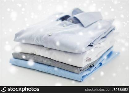 ironing, laundry, clothes, housekeeping and objects concept - close up of ironed and folded shirts on table at home over snow effect