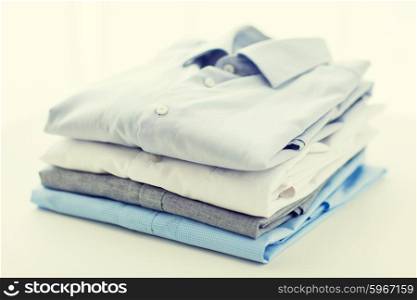 ironing, laundry, clothes, housekeeping and objects concept - close up of ironed and folded shirts on table at home