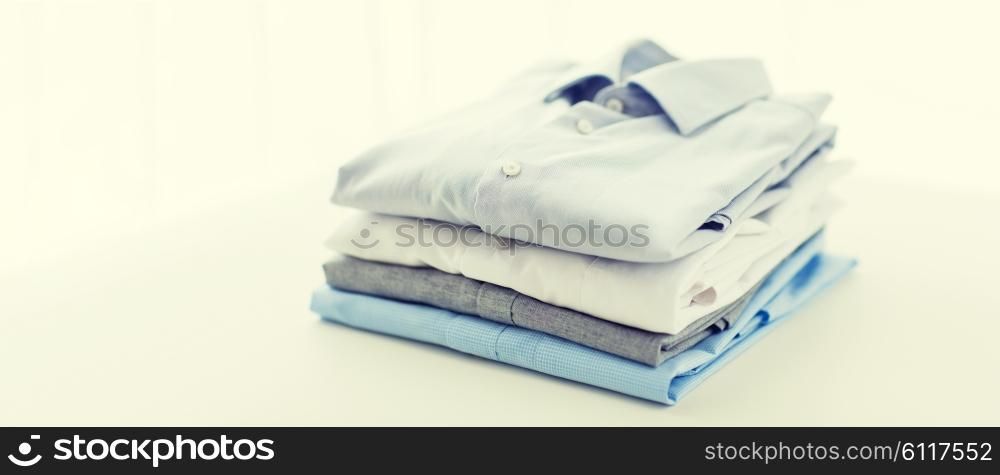ironing, laundry, clothes, housekeeping and objects concept - close up of ironed and folded shirts on table at home