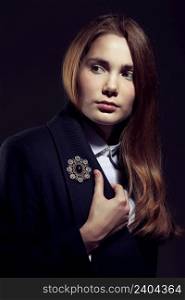 Irresistible young woman wearing a blue topcoat with a brooch on black background