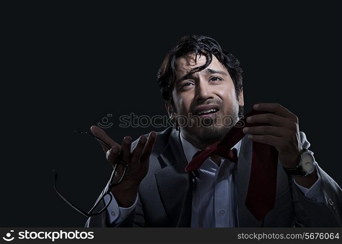 Irritated young businessman holding glasses and tie over black background