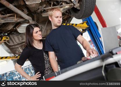 Irritated young woman standing with mechanic using laptop in garage