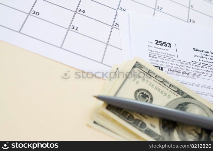 IRS Form 2553 Election by a Small Business Corporation tax blank lies with pen and many hundred dollar bills on calendar page. Tax period concept. Copy space for text. IRS Form 2553 Election by a Small Business Corporation tax blank lies with pen and many hundred dollar bills on calendar page