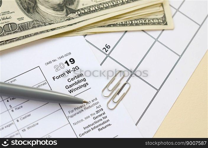 IRS Form W-2G Certain Gambling Winning blank lies with pen and many hundred dollar bills on calendar page. Tax period concept. Copy space for text. IRS Form W-2G Certain Gambling Winning blank lies with pen and many hundred dollar bills on calendar page