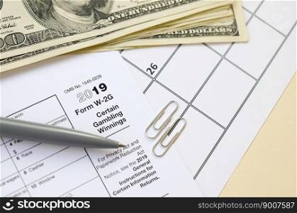 IRS Form W-2G Certain Gambling Winning blank lies with pen and many hundred dollar bills on calendar page. Tax period concept. Copy space for text. IRS Form W-2G Certain Gambling Winning blank lies with pen and many hundred dollar bills on calendar page