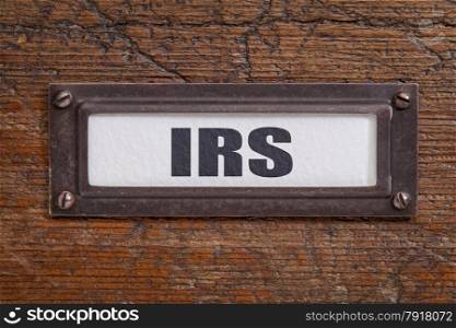 IRS - taxes concept - file cabinet label, bronze holder against grunge and scratched wood