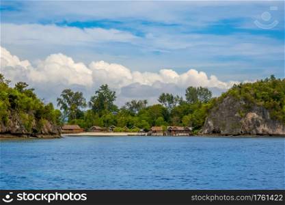 Island in indonesia. Raja Ampat. Several traditional huts on the shore between the rocks and the beach. Small Village on a Tropical Island
